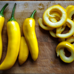 Fresh sweet and hot banana peppers on a wooden cutting board, some sliced into rings.