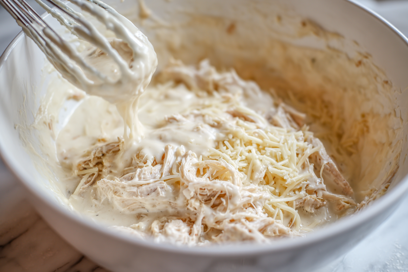 Creamy chicken Alfredo mixture being combined in a white mixing bowl.
